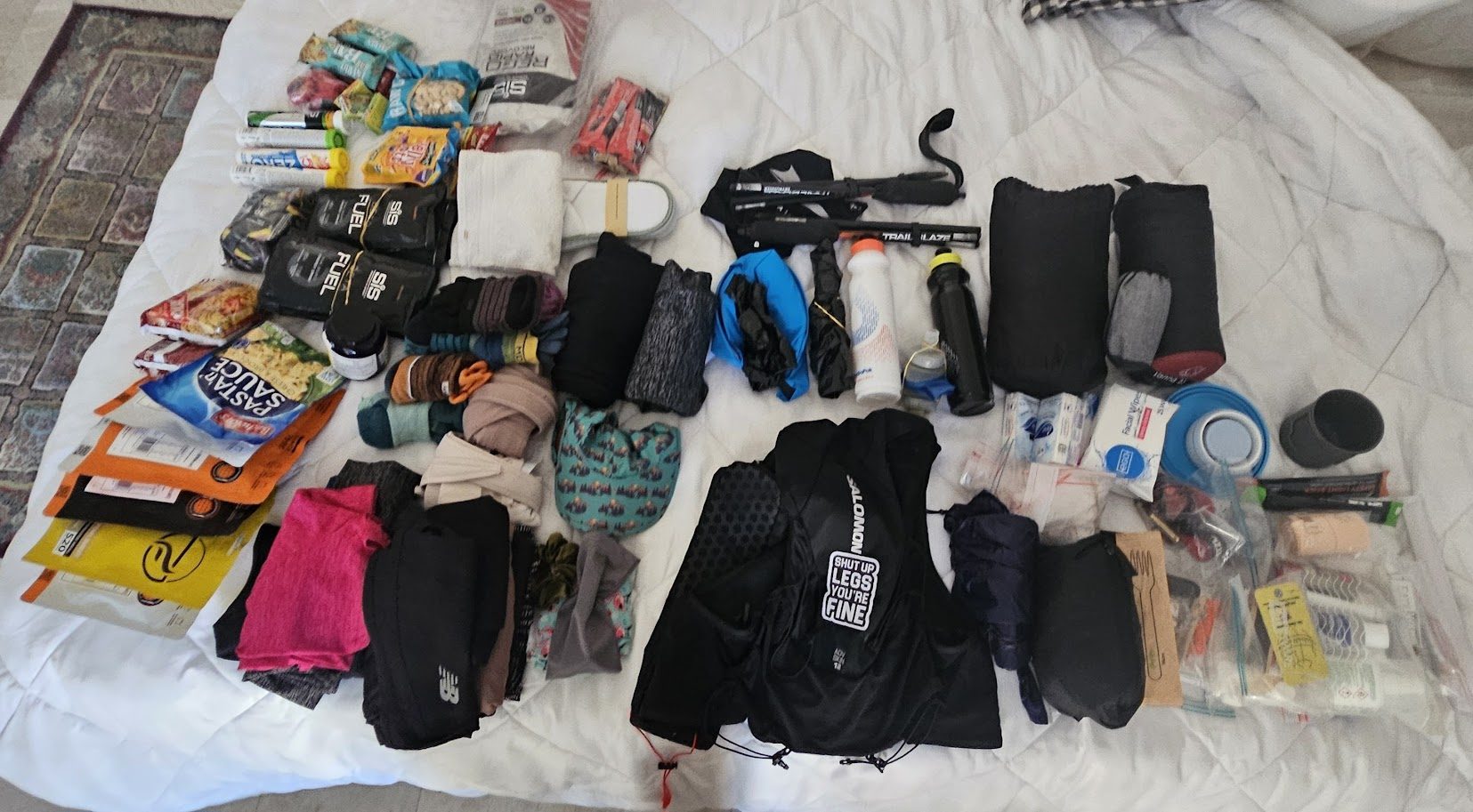 Full self-supported multi-stage race kit laid out: pack, sleeping bag, poles, mandatory gear, food, first aid