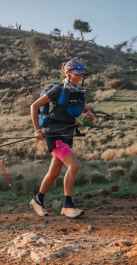Lisa running on a remote trail with poles, race kit, pink shorts