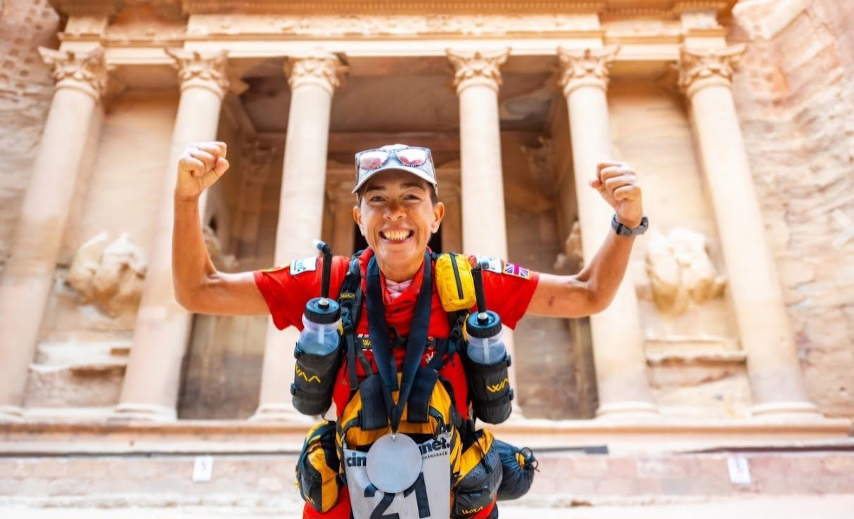 Lisa at the finish line in front of the Treasury at Petra, fists raised, finisher's medal around her neck